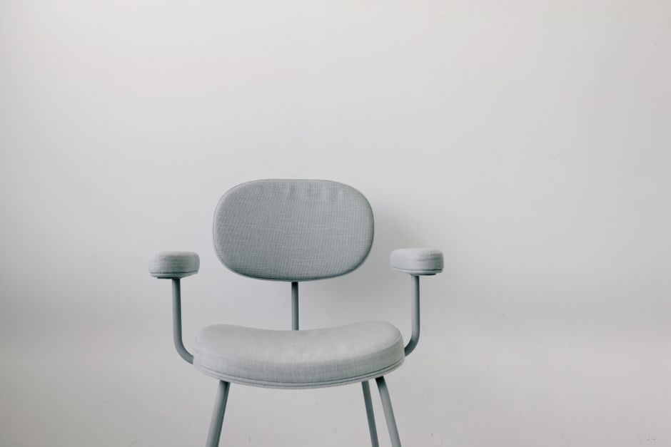 Elegant grey armchair with armrests placed in front of a sleek white wall, ideal for modern interiors.